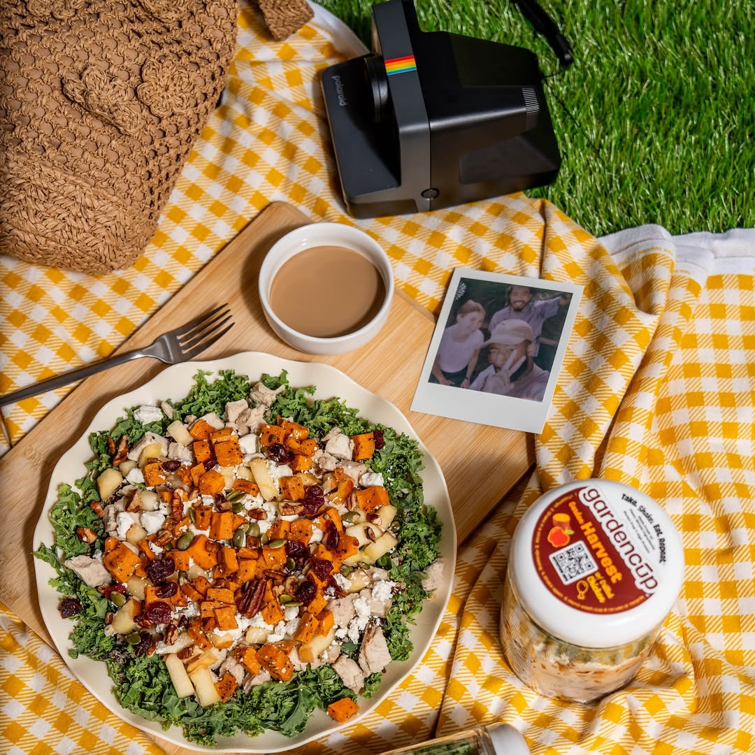 Picnic scene with salad, coffee, camera, and photo on a yellow checked blanket.