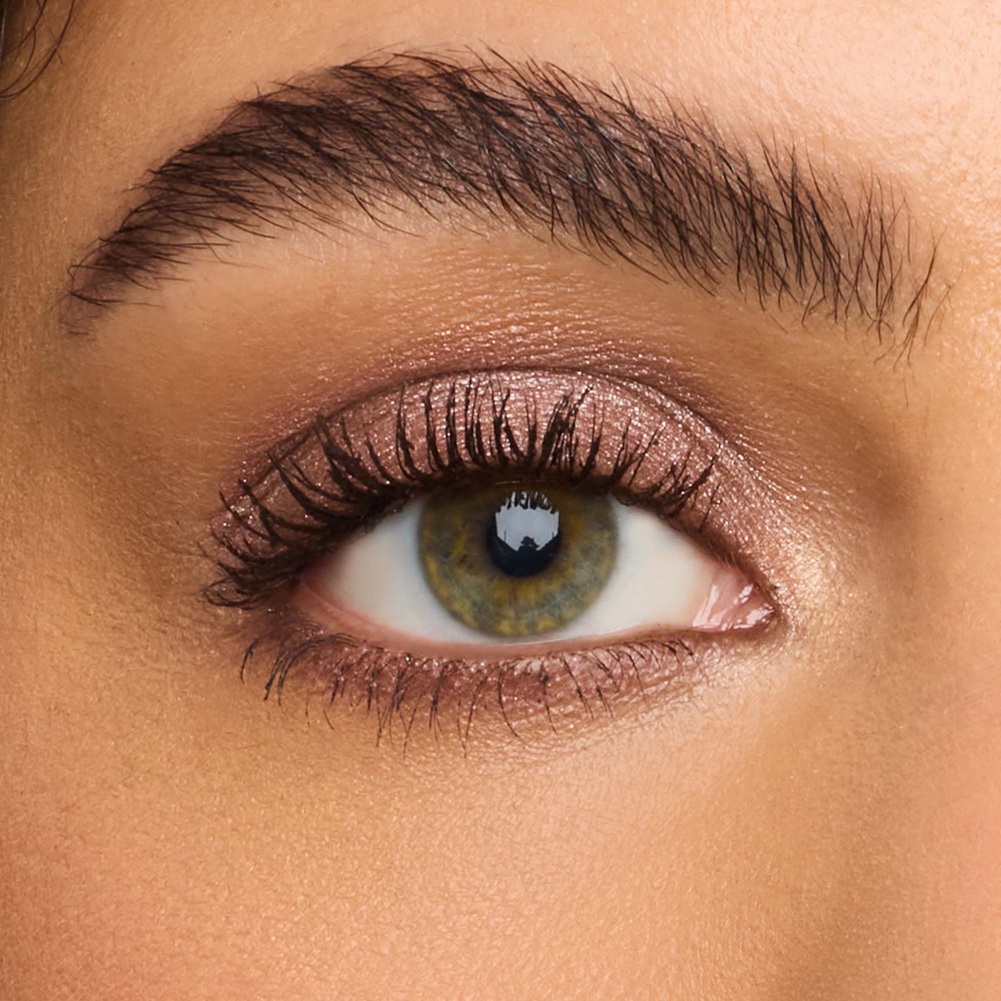 A close-up of a green eye with shimmery pinkish-brown eyeshadow and a well-defined dark eyebrow.