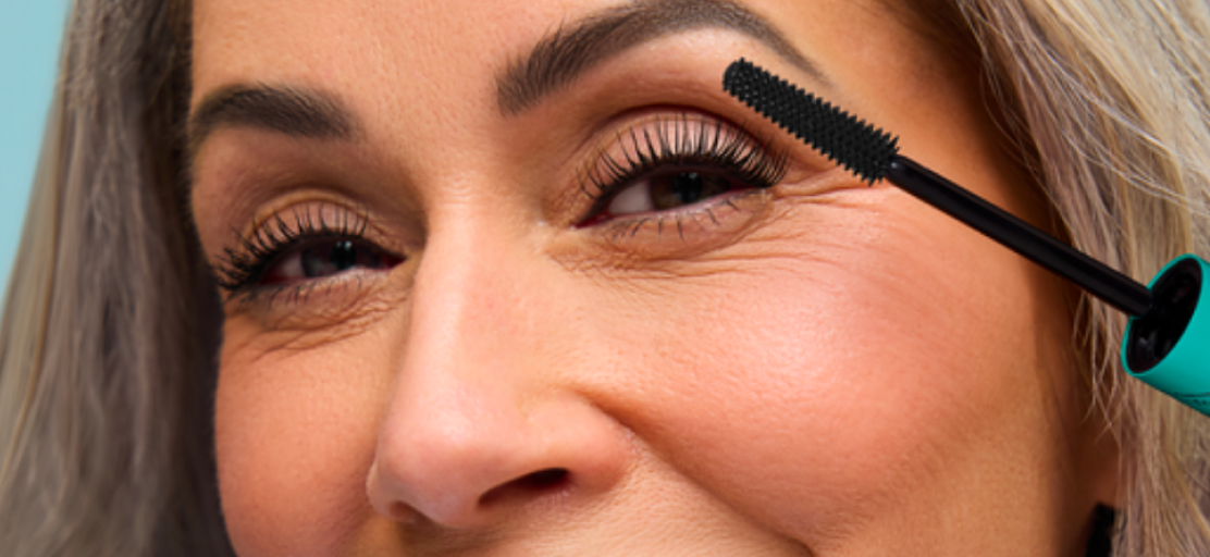 Smiling woman over 55 with silver hair applying Liquid Lash Extensions Tubing Mascara