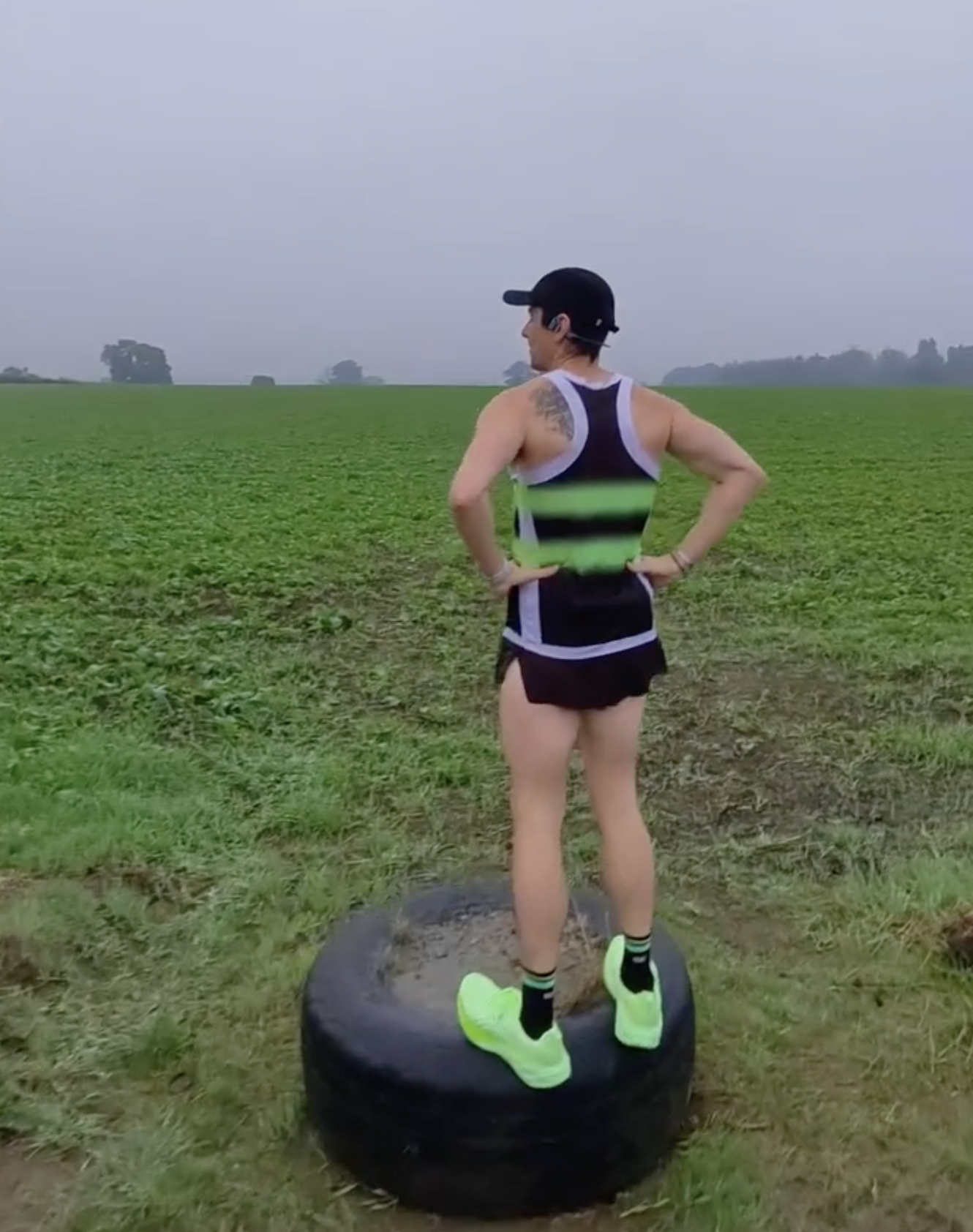 Person in athletic wear standing on a tire in a field.