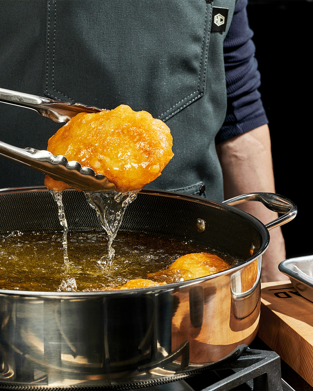 Person frying food in a pan with tongs.