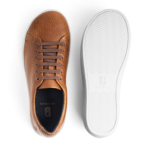 A top-down view of a brown pebbled leather sneaker next to its white rubber sole.