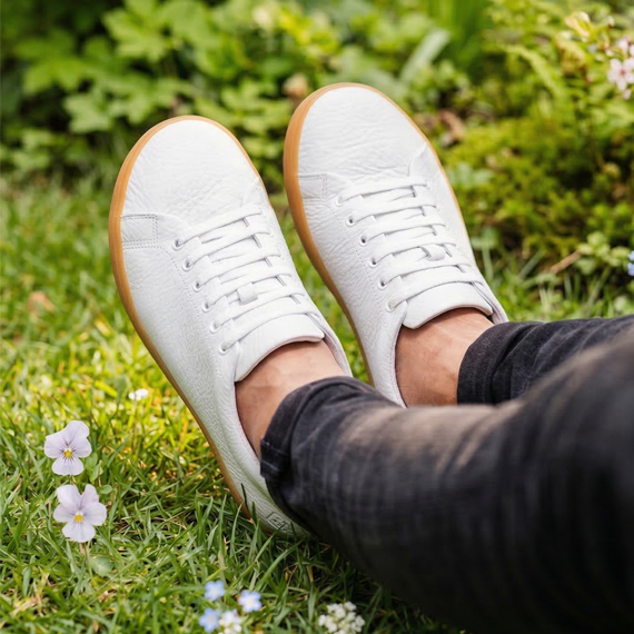 A person wearing white sneakers with gum soles sits with their feet up in a grassy field.