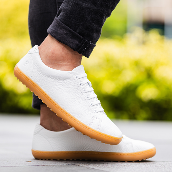 A close-up of a person wearing white leather sneakers with gum soles and cuffed black pants.
