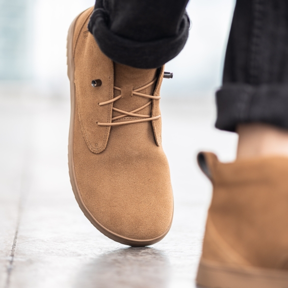 Close-up of a person wearing brown suede shoes on a concrete surface.