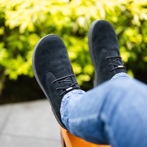 Person wearing black shoes and jeans, relaxing outdoors on a bench.