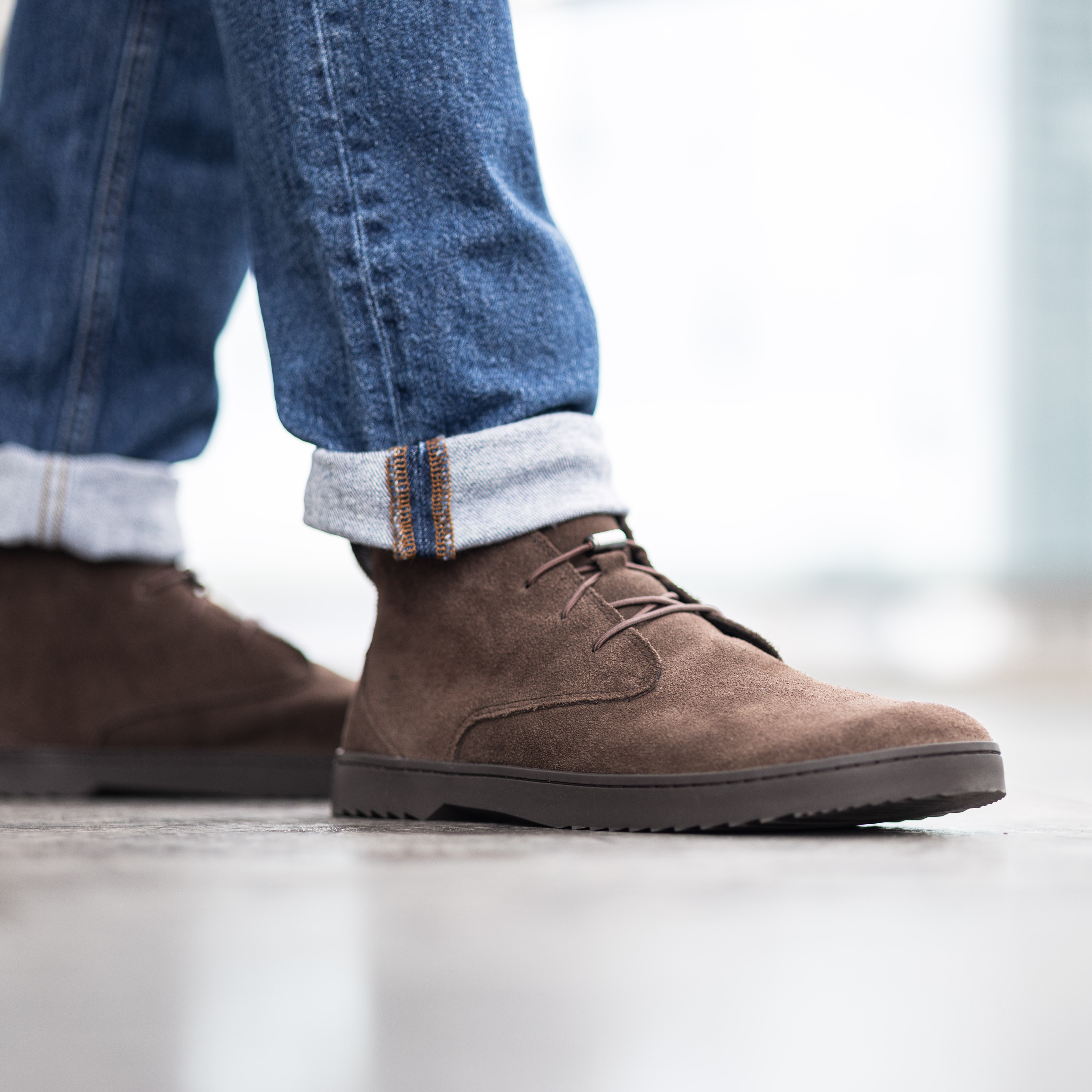 Person wearing brown suede shoes and rolled-up blue jeans.