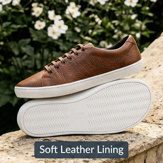A brown leather sneaker with a white sole rests on top of another shoe's sole outdoors.