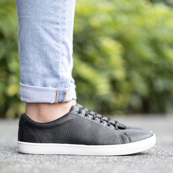 A close-up of a person wearing black leather sneakers with a white sole and rolled-up blue jeans.