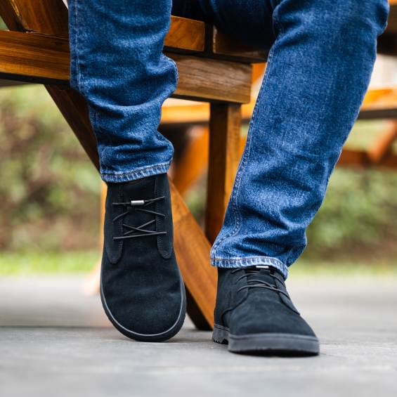 Person wearing black shoes and blue jeans sitting on a wooden bench.
