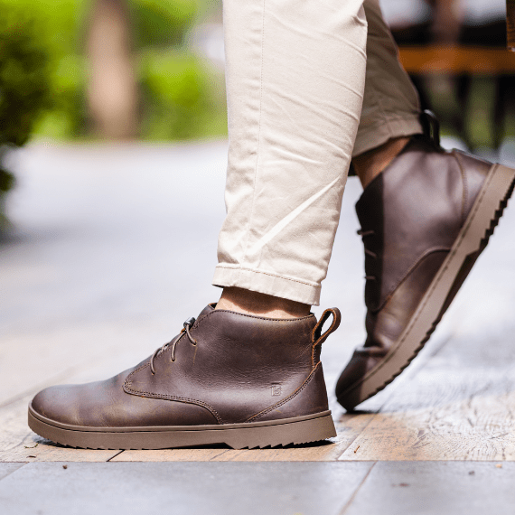 Person wearing brown leather boots and beige pants on a wooden floor.