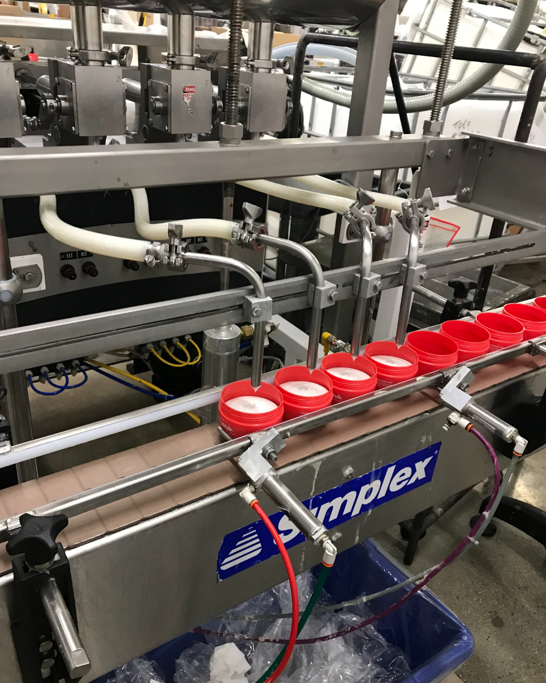 Industrial filling machine with red-lidded containers on a conveyor belt.