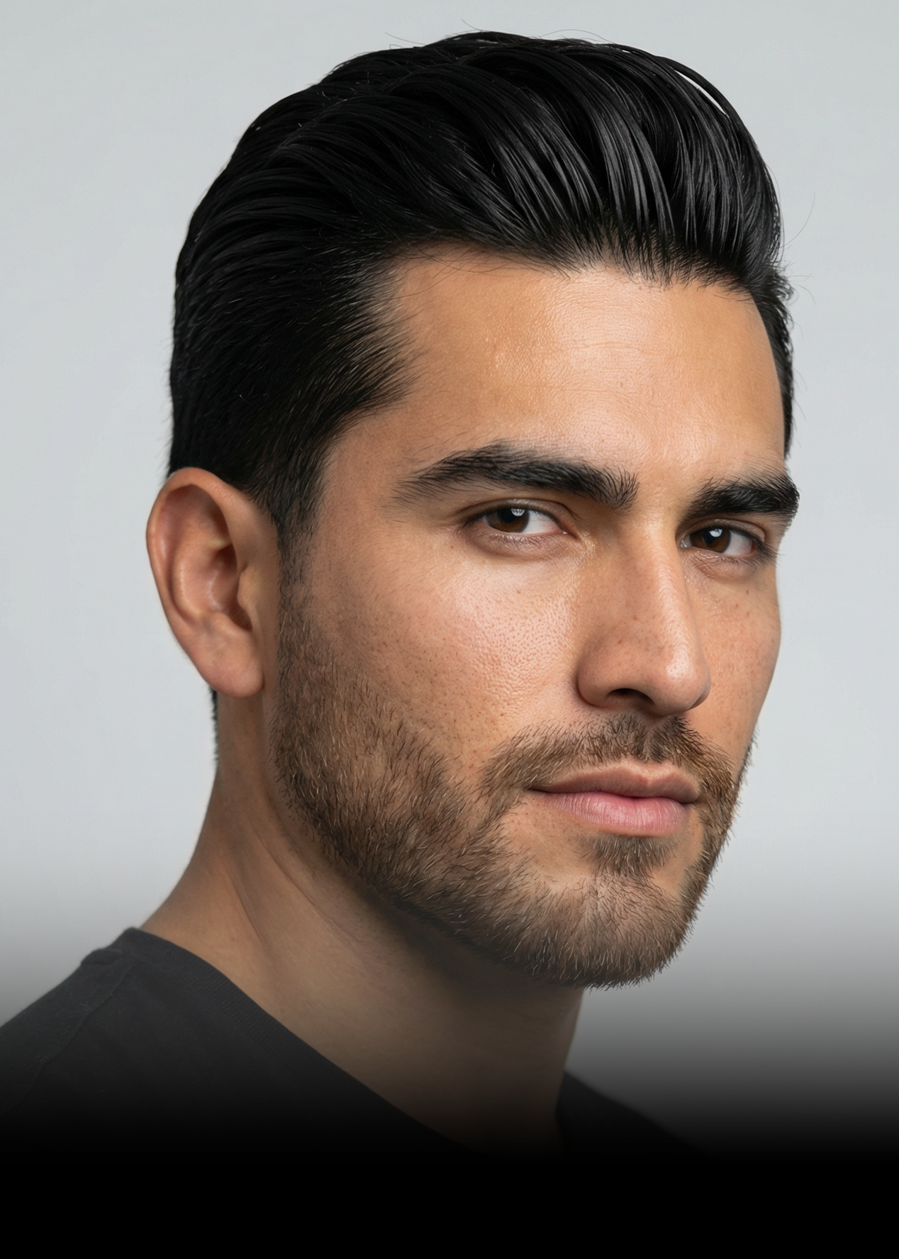 A close-up headshot of a man with dark styled hair and a short beard looking at the camera.
