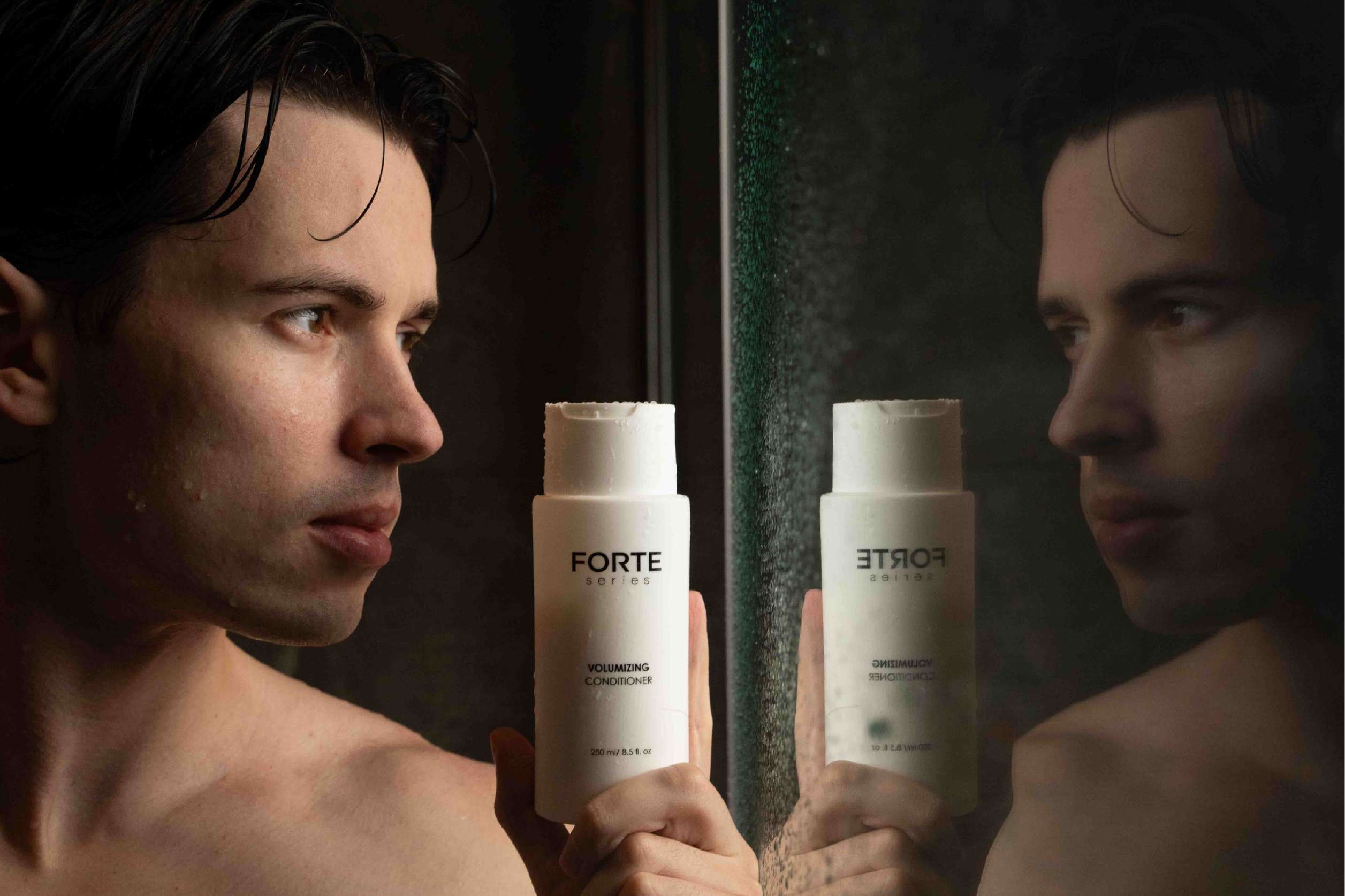Person holding Forte conditioner bottle in front of a mirror.
