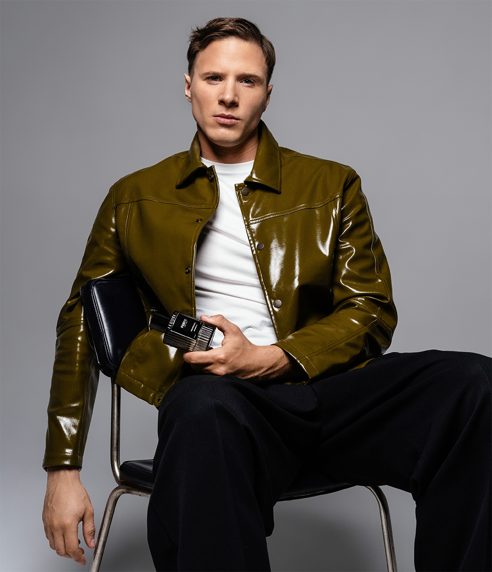 Person in green jacket holding a black bottle, sitting on a chair.