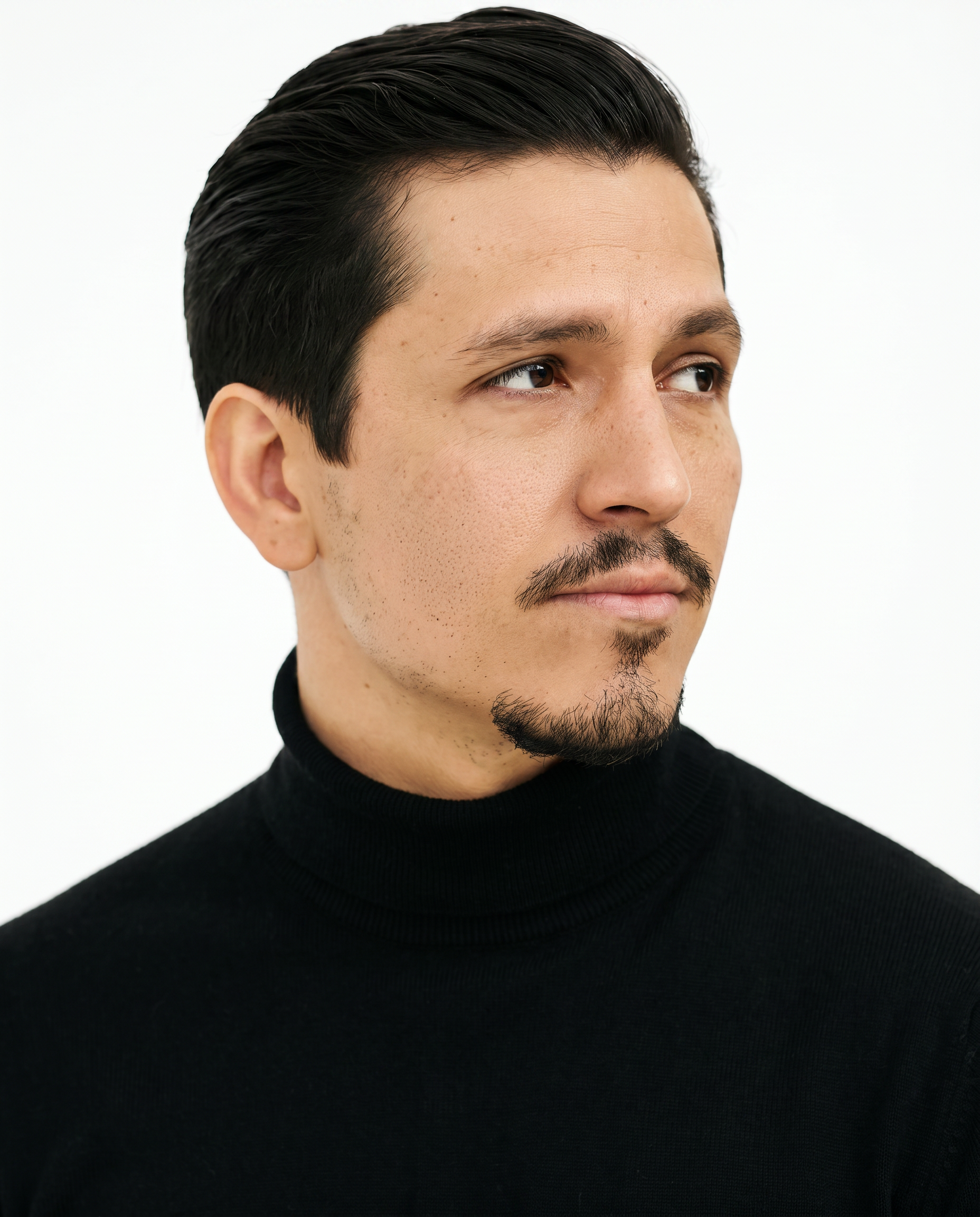 A man with a mustache and goatee wearing a black turtleneck looks off to the side.