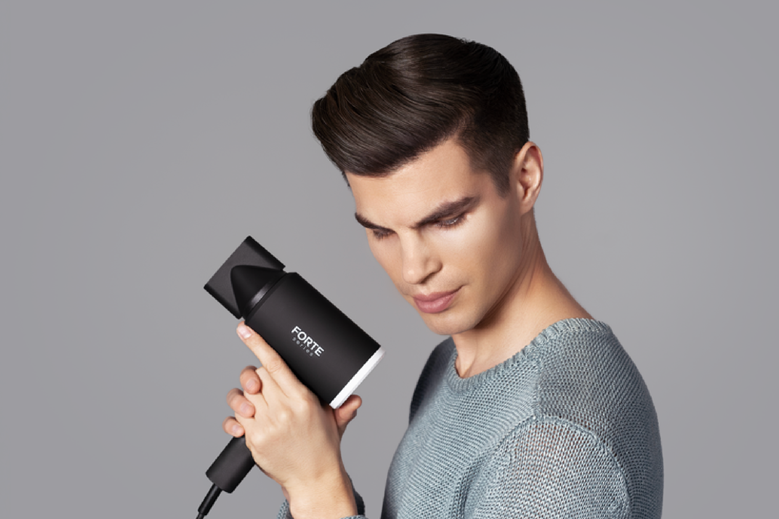 Person holding a black hairdryer against a gray background.