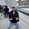 Person posing energetically on a rooftop with modern architecture in the background.