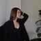 Person sitting indoors, looking to the side, with a plant in the background.