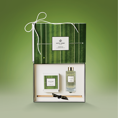 A Hotel Lobby Home gift set with a reed diffuser and candle in an open green striped box.