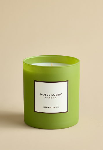 A Hotel Lobby 'Racquet Club' soy candle in a matte, light green glass jar.