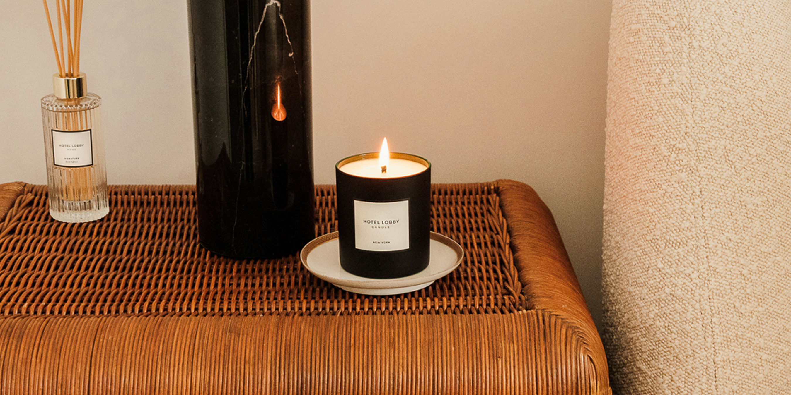 Lit candle and diffuser on a wicker table.