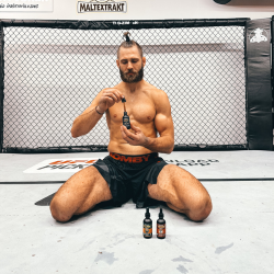 Man sitting on gym mat holding dropper bottle, two more bottles in front.