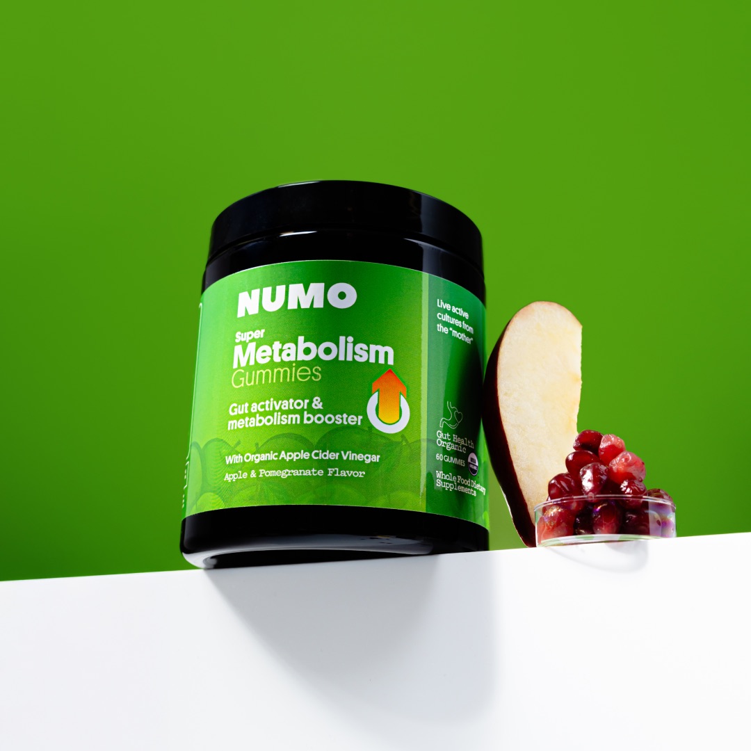 Jar of metabolism gummies with apple slice and pomegranate seeds on green background.