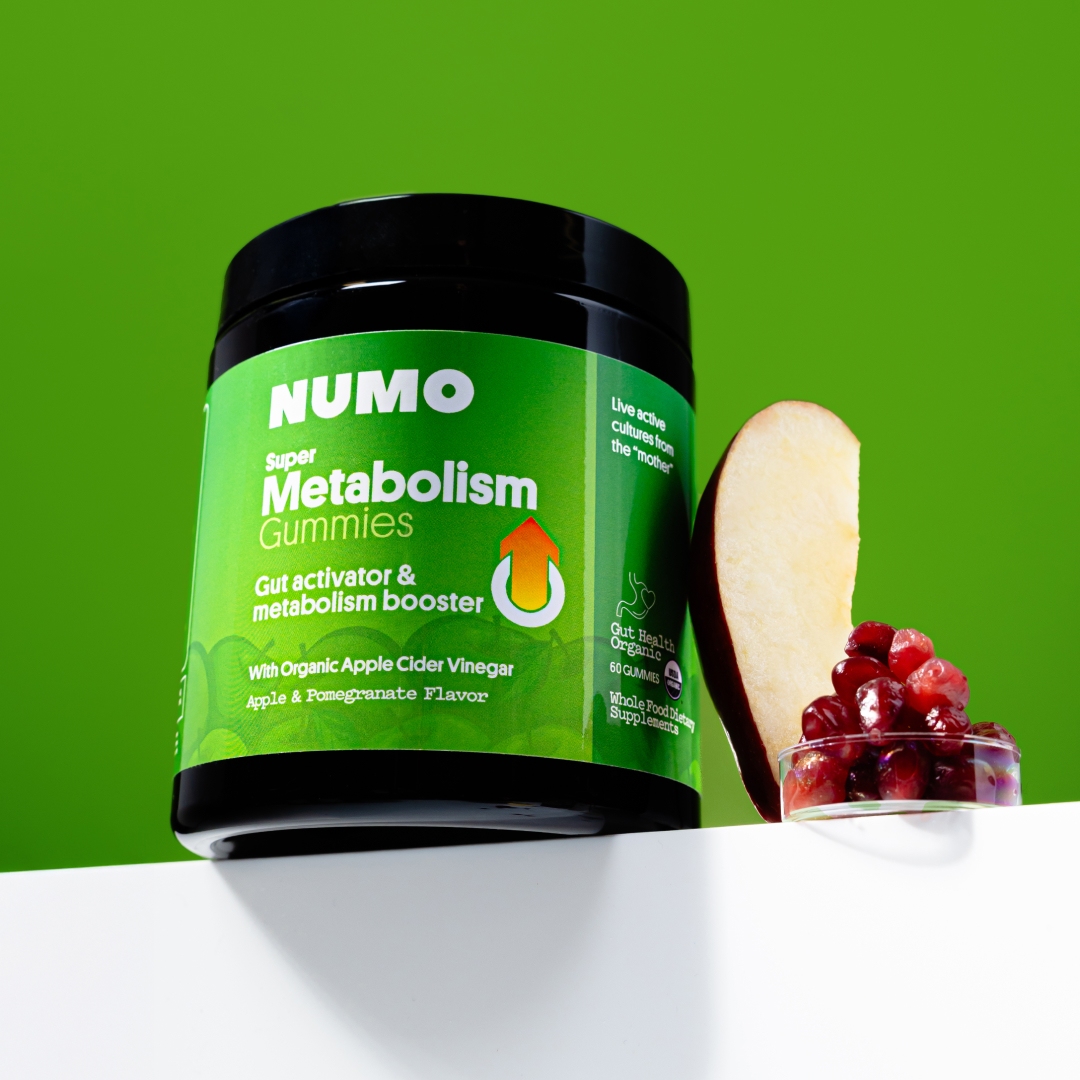 Jar of metabolism gummies with apple slice and pomegranate seeds on green background.