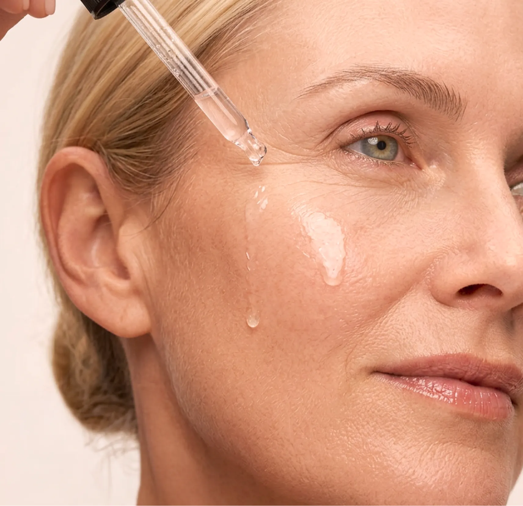 A close-up of a clear liquid being applied to a woman's face with a dropper.
