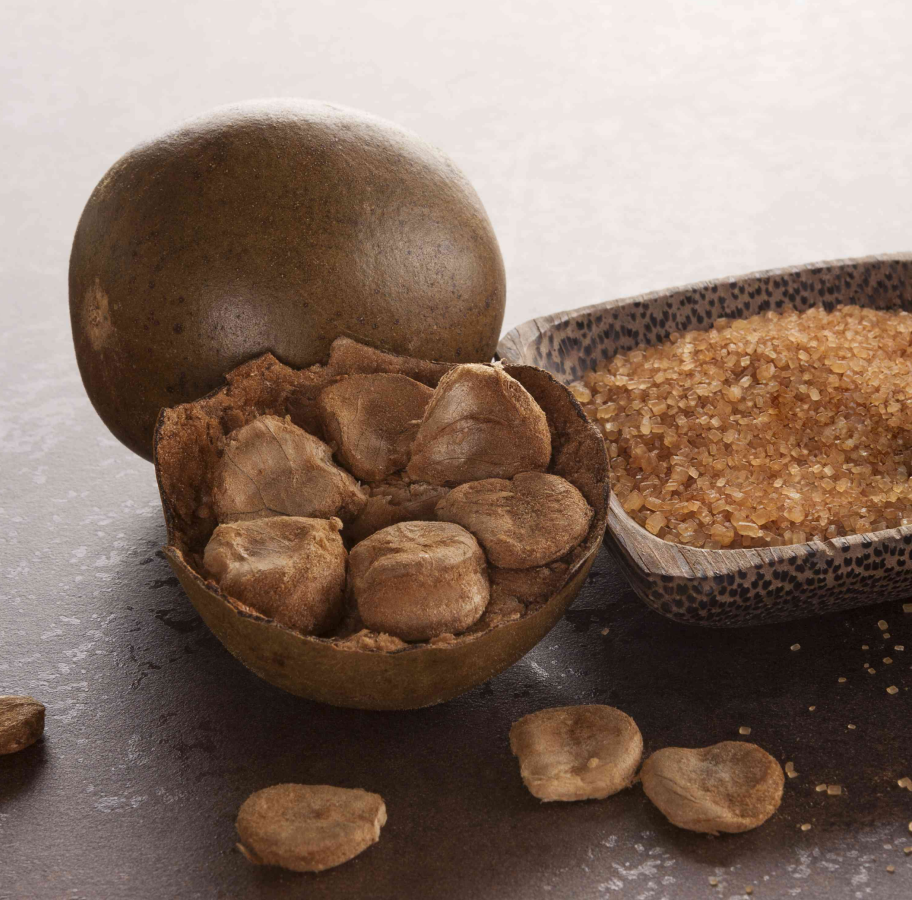 Open monk fruit with seeds and a bowl of brown sugar on a dark surface.