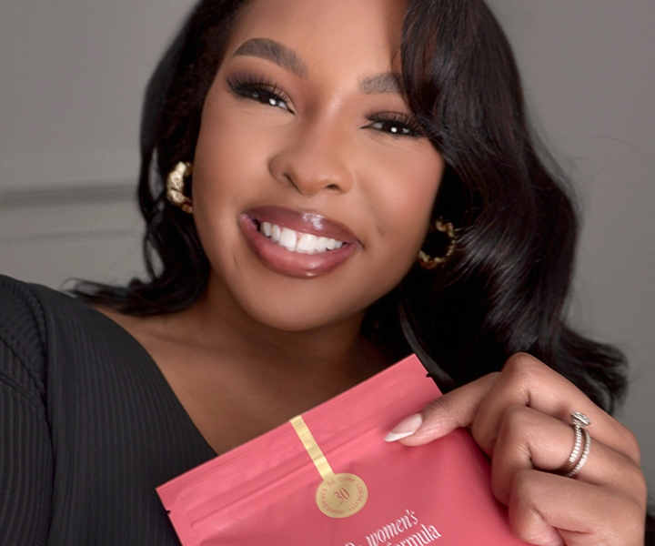 Person smiling, holding a red product package with gold detail.