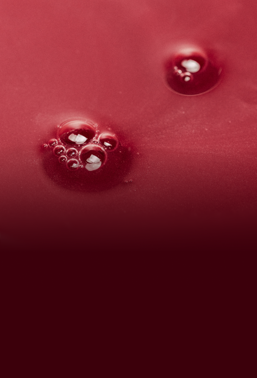 A macro shot of bubbles resting on the surface of a viscous red liquid.