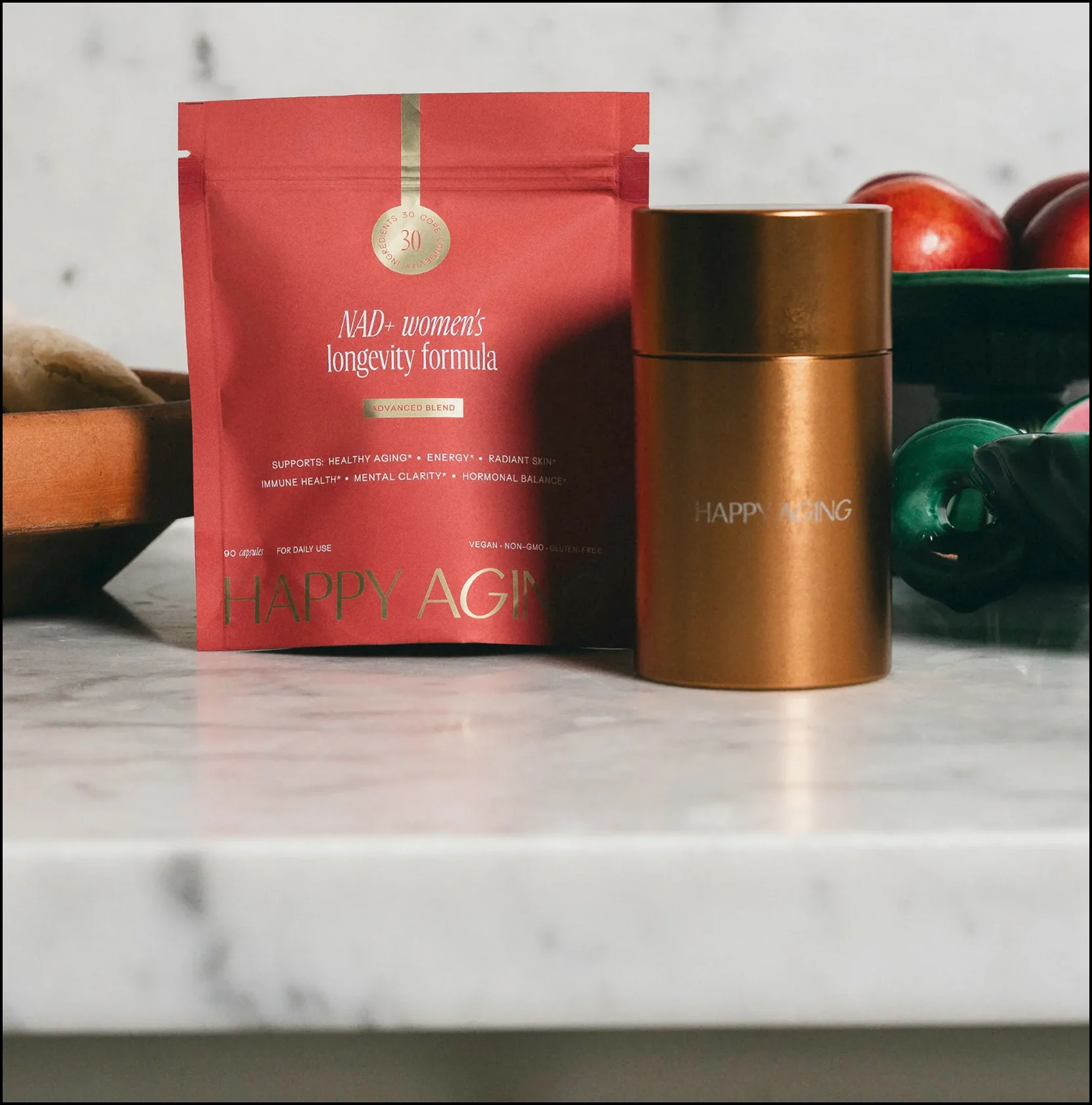 Red and gold skincare packaging on marble counter with fruit background.