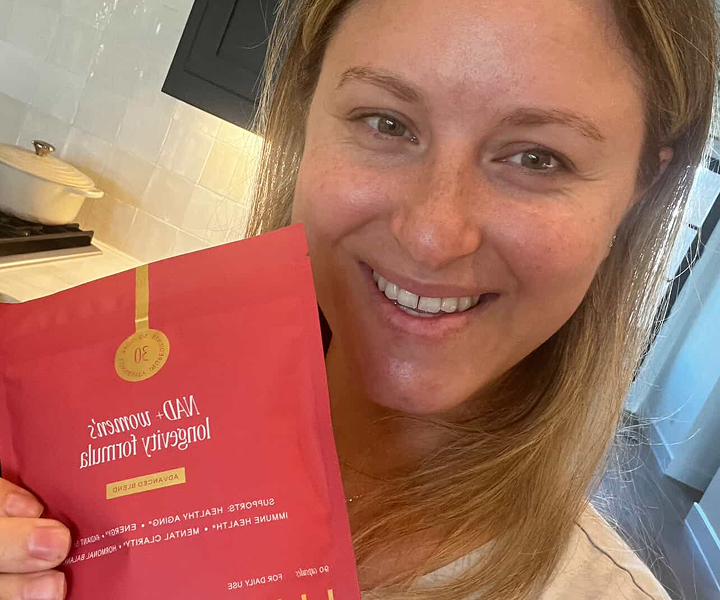 Person holding a red longevity supplement packet in a kitchen.