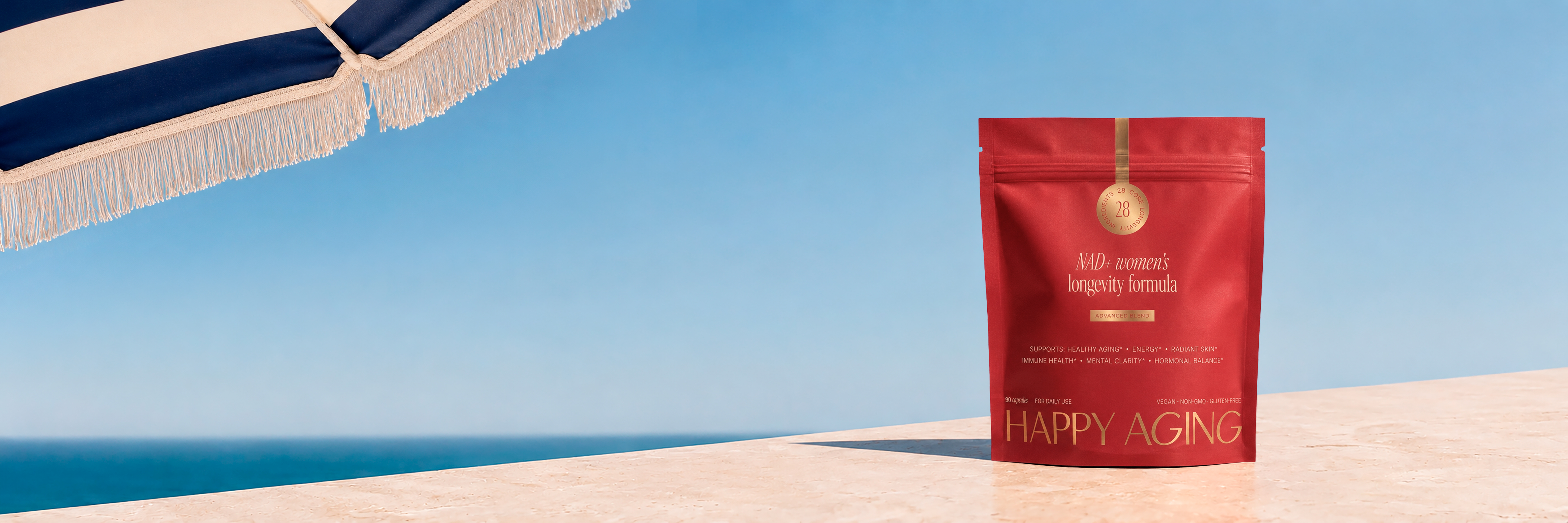 A red pouch of Happy Aging supplement sits on a ledge by the sea under a beach umbrella.