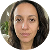 A circular headshot of a woman with dark wavy hair and brown eyes looking at the camera.
