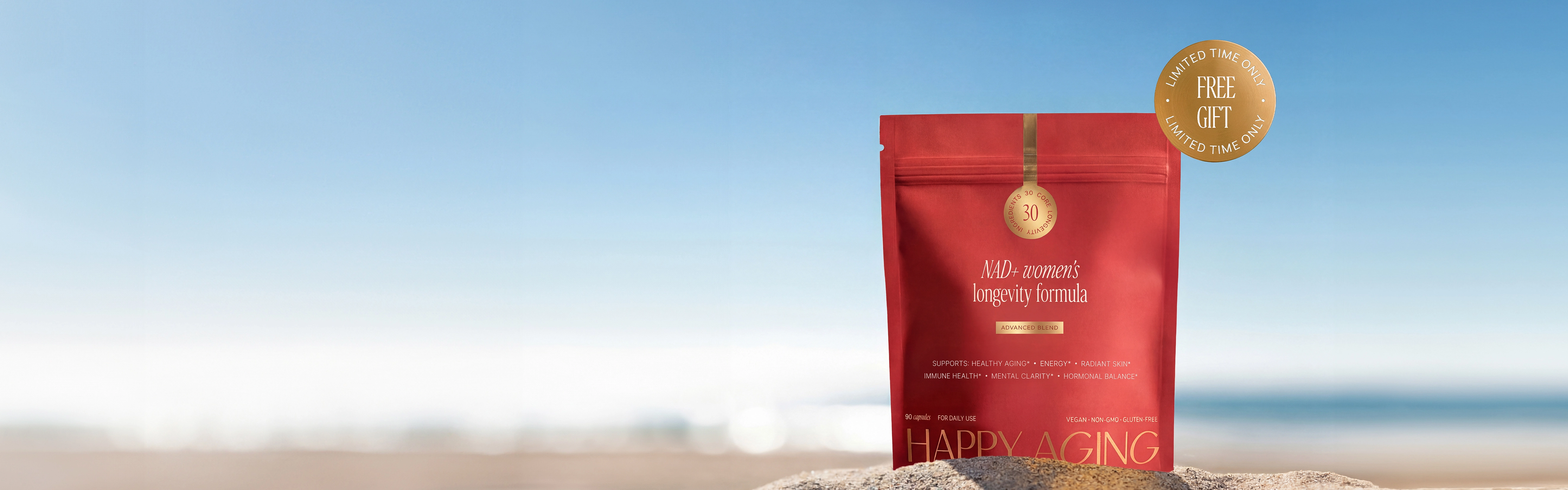 A red pouch of Happy Aging longevity formula sits in the sand on a beach.