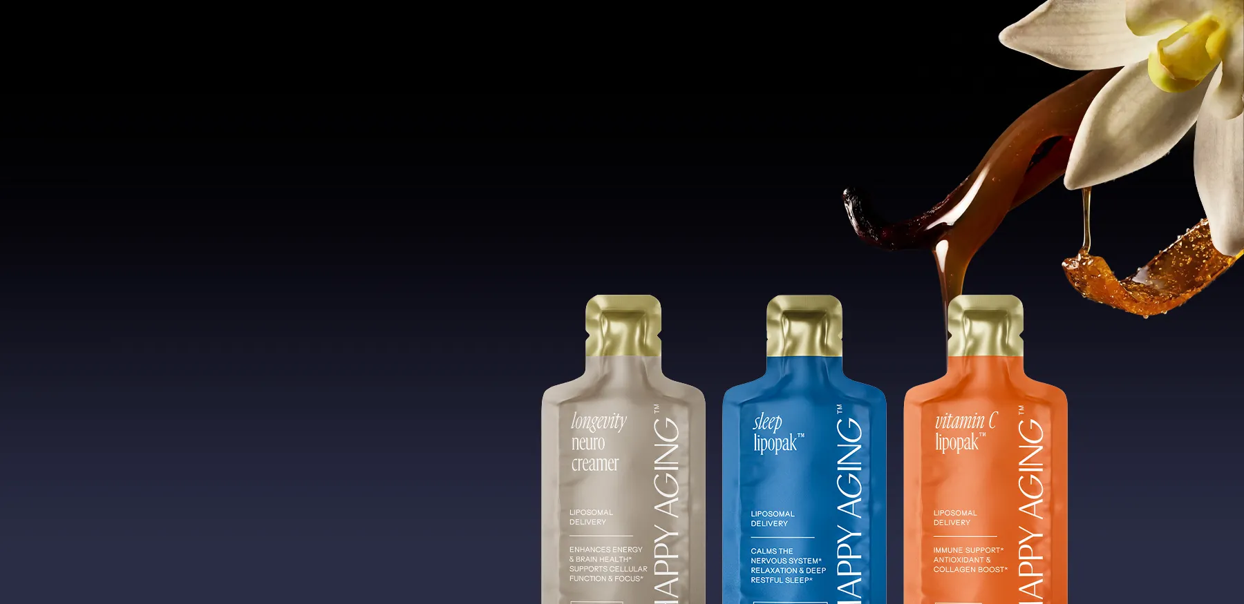 Syrup from a vanilla bean drips onto three colorful 'Happy Aging' supplement packets below a white flower.