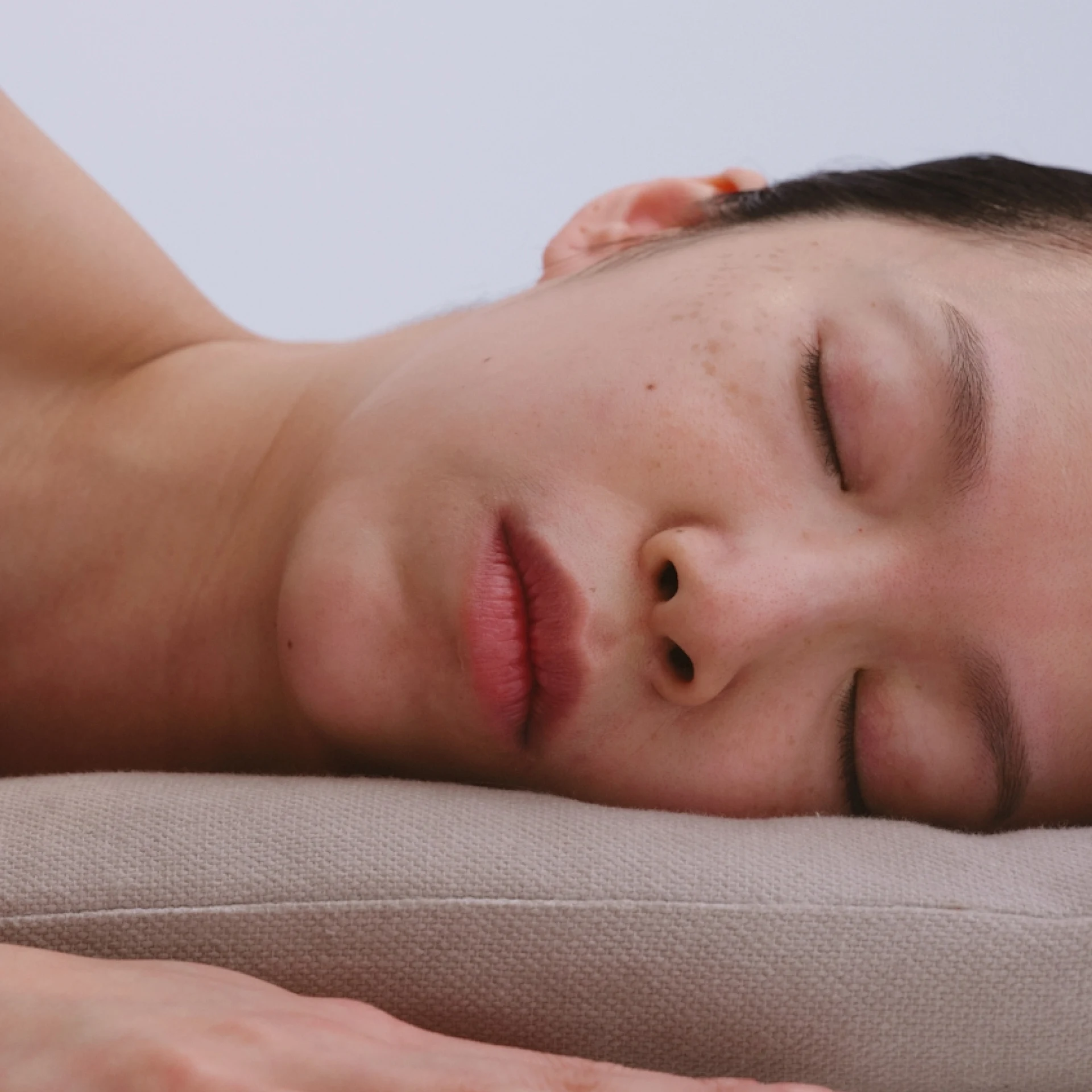Person sleeping on a beige pillow with eyes closed.