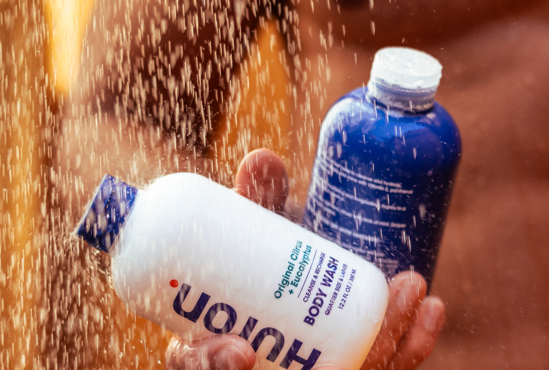 Two bottles of body wash held under a shower.