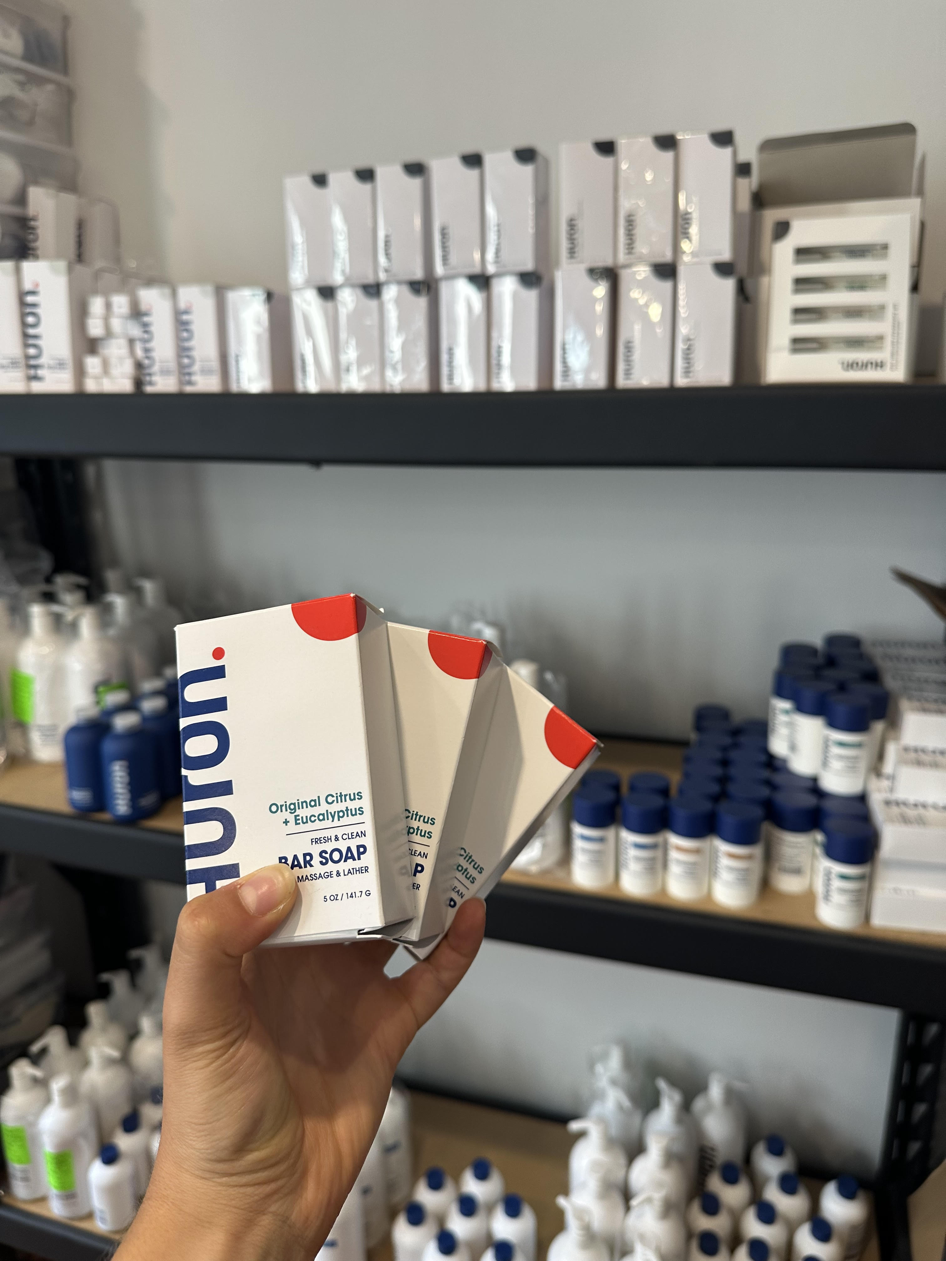 Hand holding three bar soap boxes in front of shelves with various products.