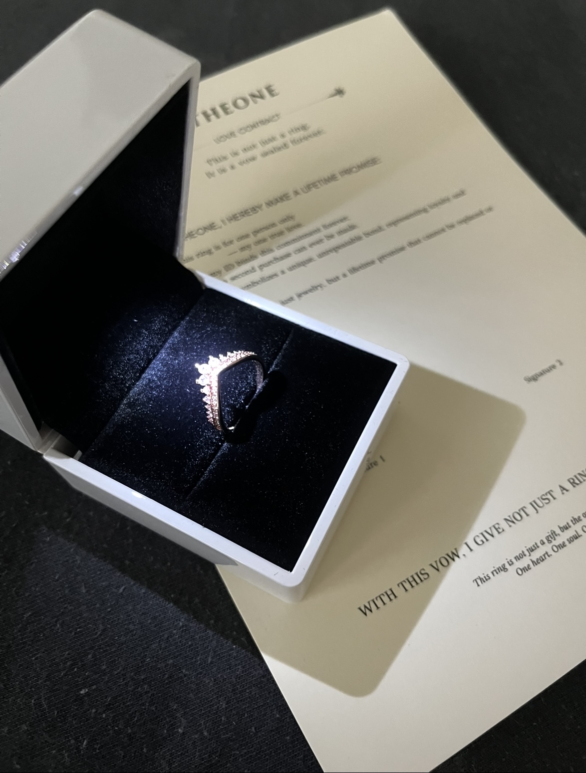 An ornate ring in a box with a document underneath.