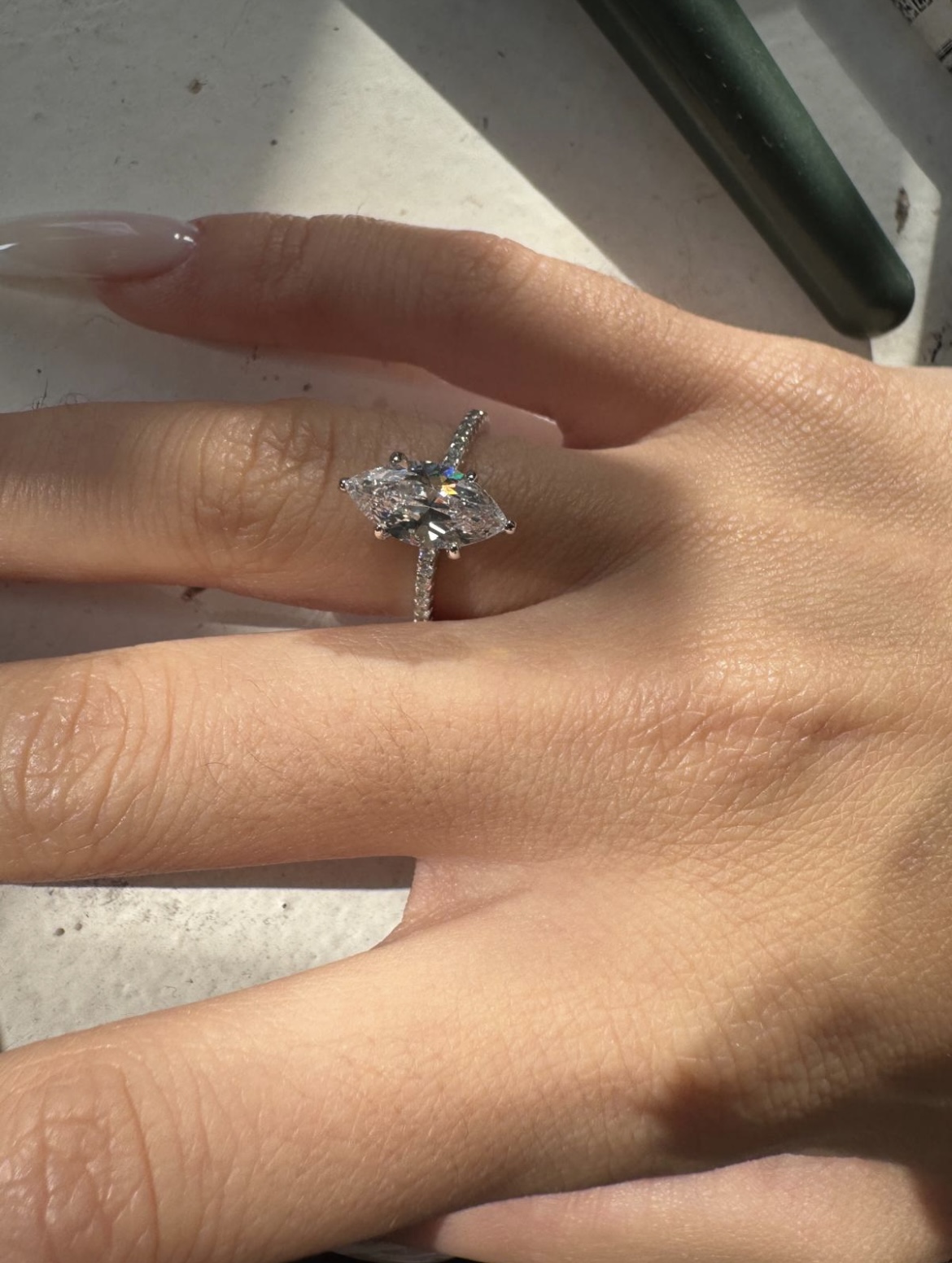A hand wearing a diamond ring with a marquise-cut stone.