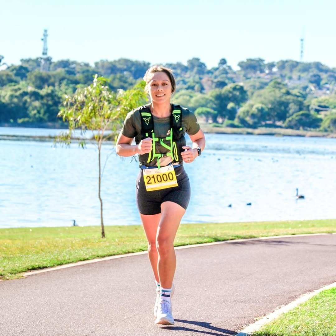 Person running on a lakeside path with a race bib.