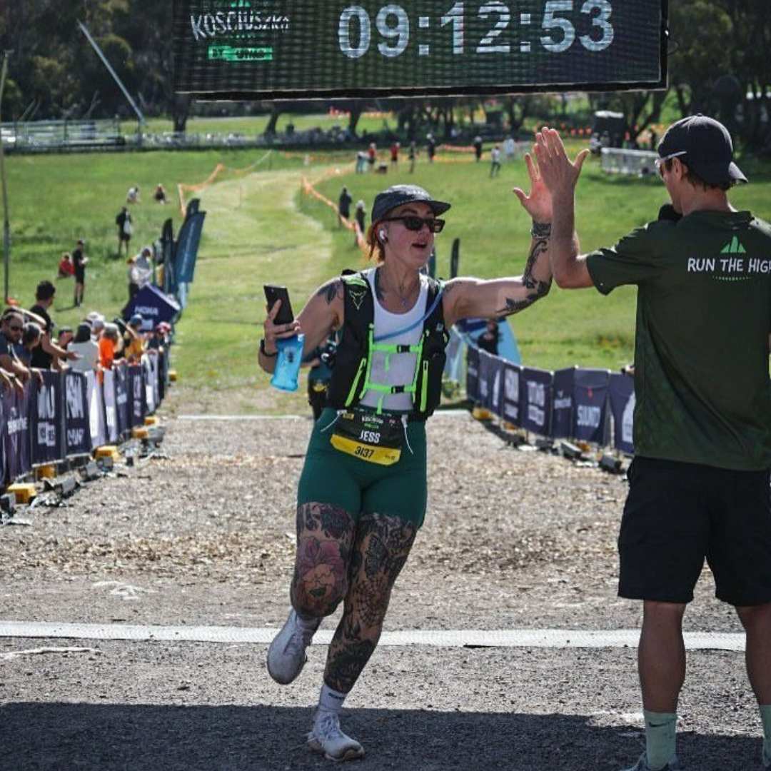 Woman high-fiving man at finish line, wearing race gear, timer showing 09:12:53.
