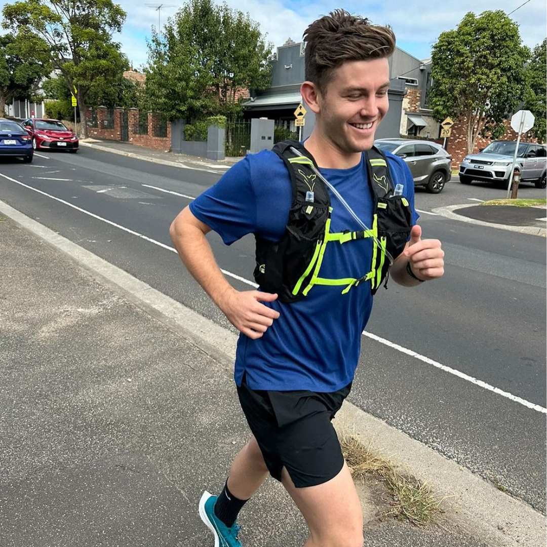 Person jogging on a sidewalk, wearing a blue shirt and running vest.