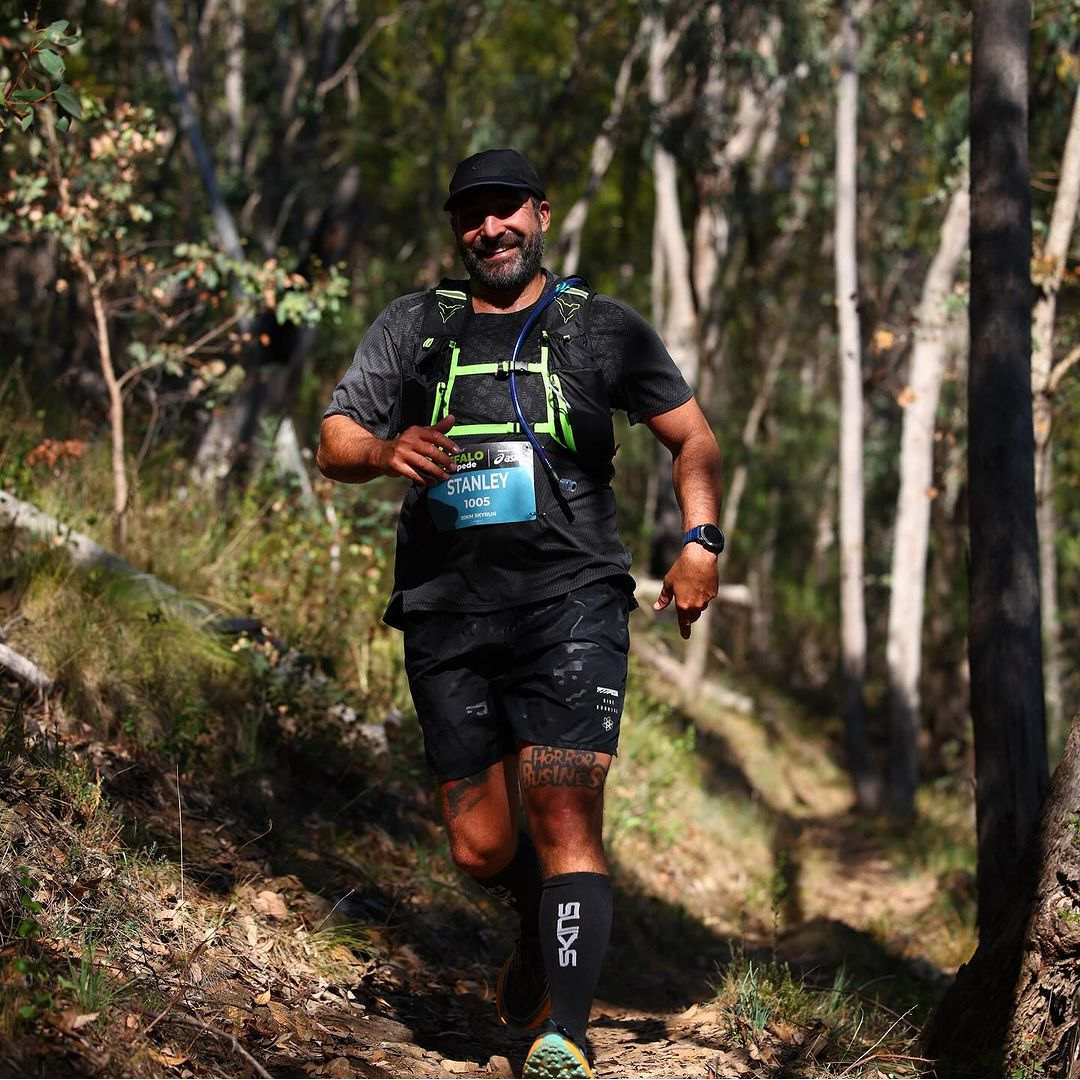 Person running on a forest trail wearing a race bib.