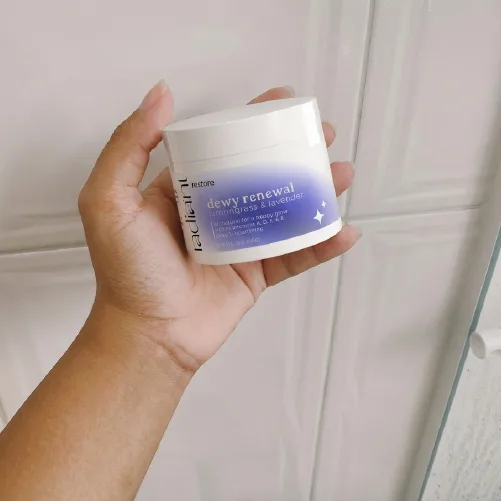 Hand holding a dewy renewal cream jar against a wall.