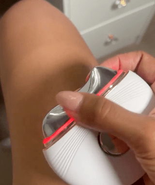 Hand holding a white and silver device near a leg.